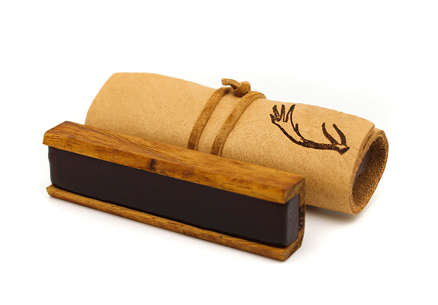The Leatherwood Bespoke features a rectangular wax or ink stick in a wooden holder beside a rolled brown paper or leather tied with cord and stamped with an antler design, both set against a white background.