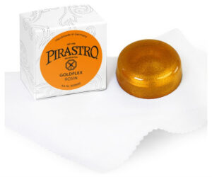 A round, golden Pirastro Goldflex Viola Rosin rests on a white cloth beside its white box with an orange label and decorative patterns, indicating it's handmade in Germany for string instruments.